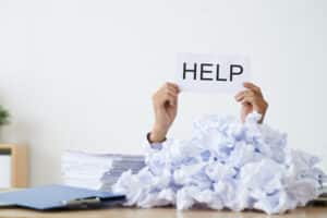 Blog image person under heap of crumpled papers with hand holding a help sign