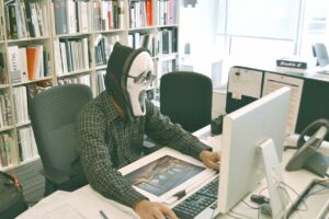 Person wearing scream mask in front of computer
