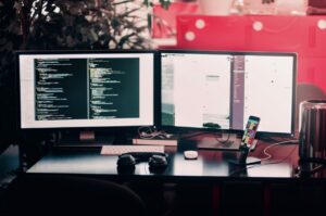 Computer with two monitors with code and headphones on desk