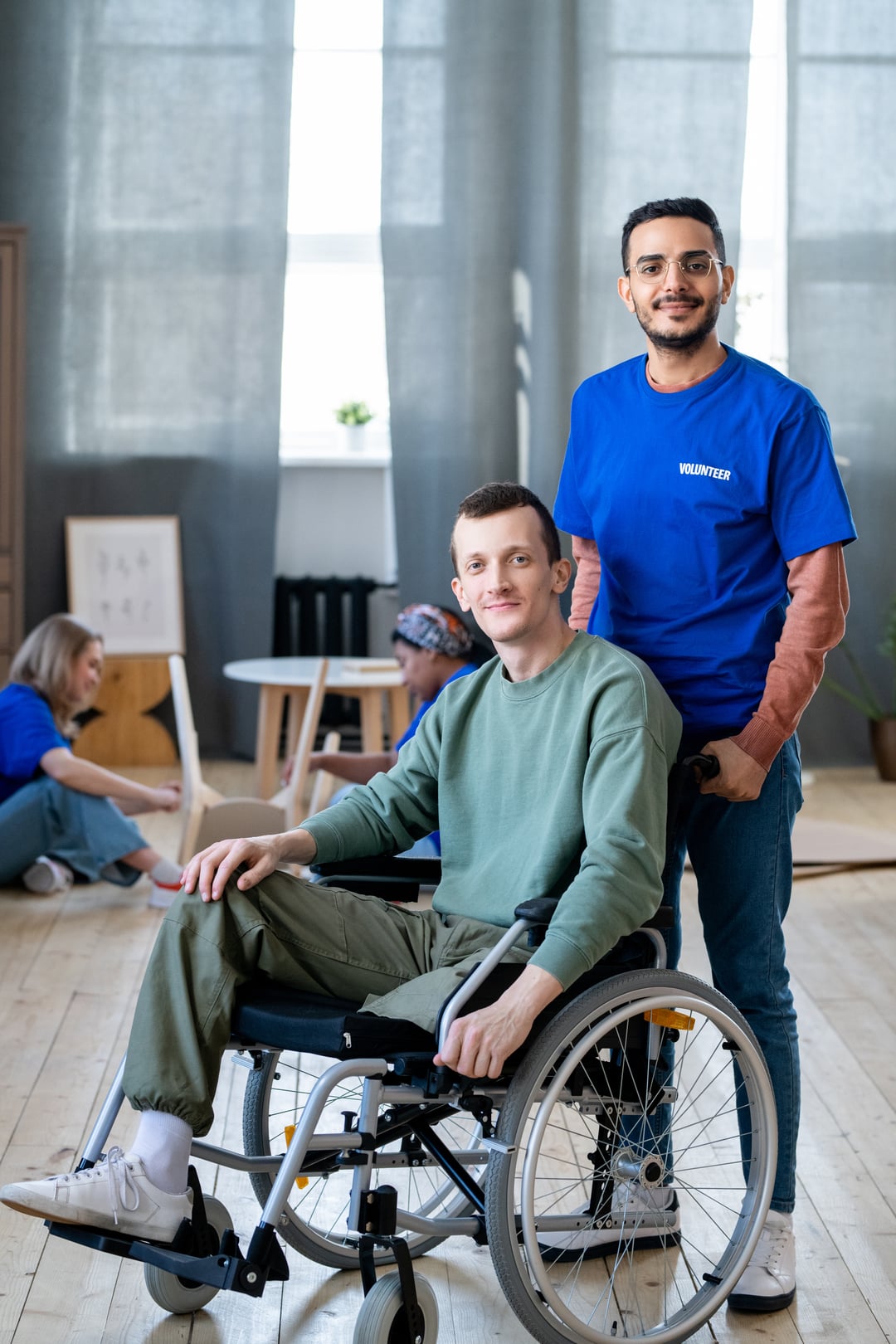 Young male volunteer standing next to man in a wheelchair