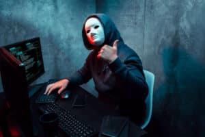 Masked hacker giving thumbs up in front of computer