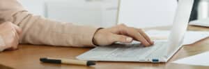 Hand placed on top of laptop keyboard next to pen