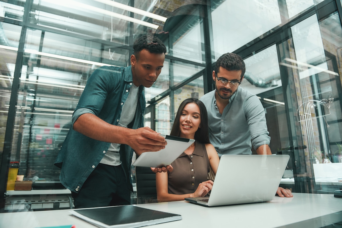 Three happy people looking at laptop in modern office