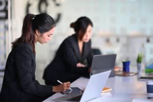 Two businesswomen working and practicing endpoint protection in a modern office setting