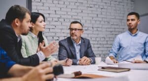 group of coworkers in meeting room sitting at the desk, mid-discussion